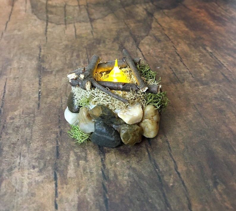 May include: A miniature campfire with a glowing LED light, surrounded by small rocks and moss.