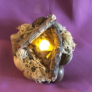 May include: A small, decorative tabletop fire pit made of wood, rocks, and moss. The fire pit has a small, yellow LED light in the center.