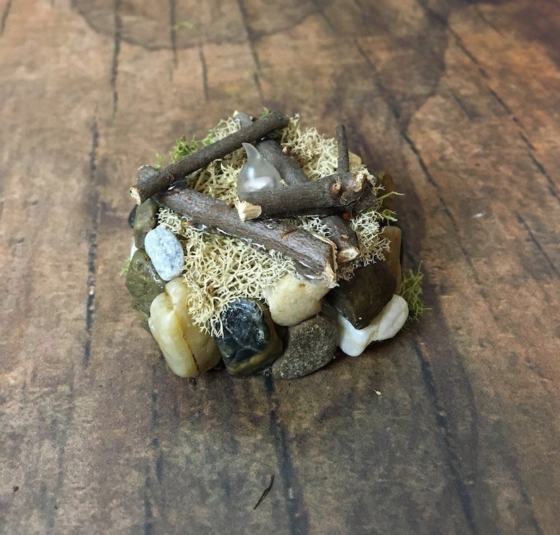 May include: A miniature campfire made of small twigs, rocks, and moss. A small white light bulb is placed in the center of the campfire.