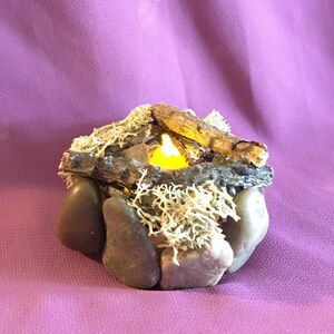 May include: A small, decorative campfire made of rocks, twigs, and moss with a glowing LED candle in the center.