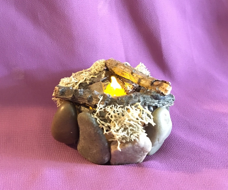 May include: A small, decorative campfire made of rocks, twigs, and moss with a glowing LED candle in the center.