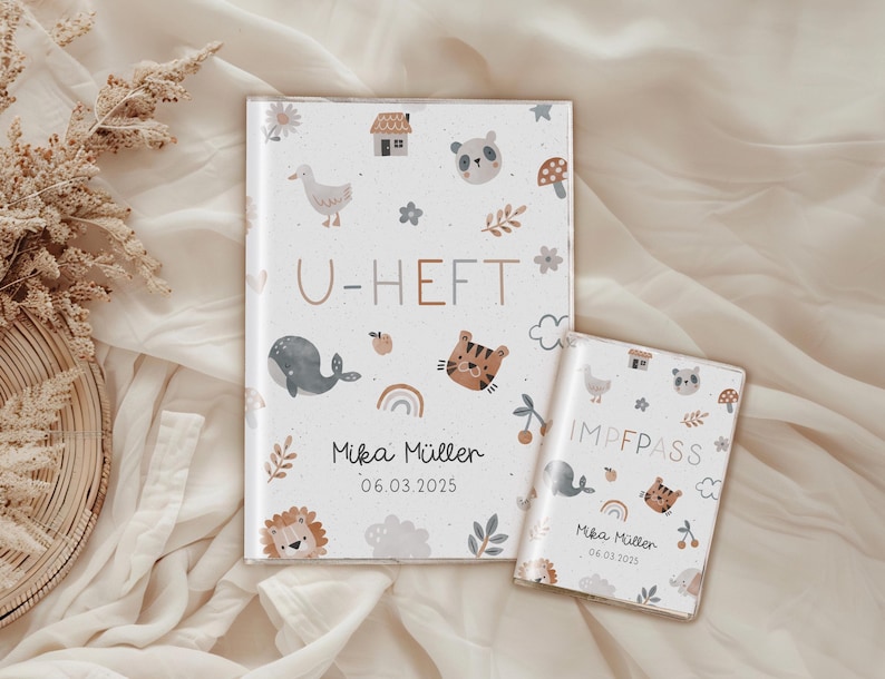 May include: Two white baby books with a colorful animal and nature pattern. The larger book says "U-HEFT" and the smaller book says "IMPFPASS". Both books have the name "Mika M&uuml;ller" and the date "06.03.2025" printed on them.