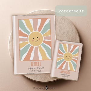 Könnte beinhalten: Zwei hellrosa Dokumentenhalter mit einem lächelnden Sonnendesign. Der größere Halter trägt die Aufschrift "U-HEFT" mit einem Namen und Datum. Der kleinere Halter trägt die Aufschrift "IMPFPASS" mit demselben Namen und Datum. Das Sonnendesign hat Pastellfarben.
