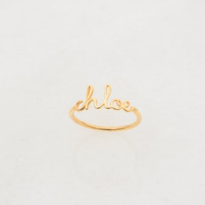 May include: A gold ring with the word "chloe" written in cursive.
