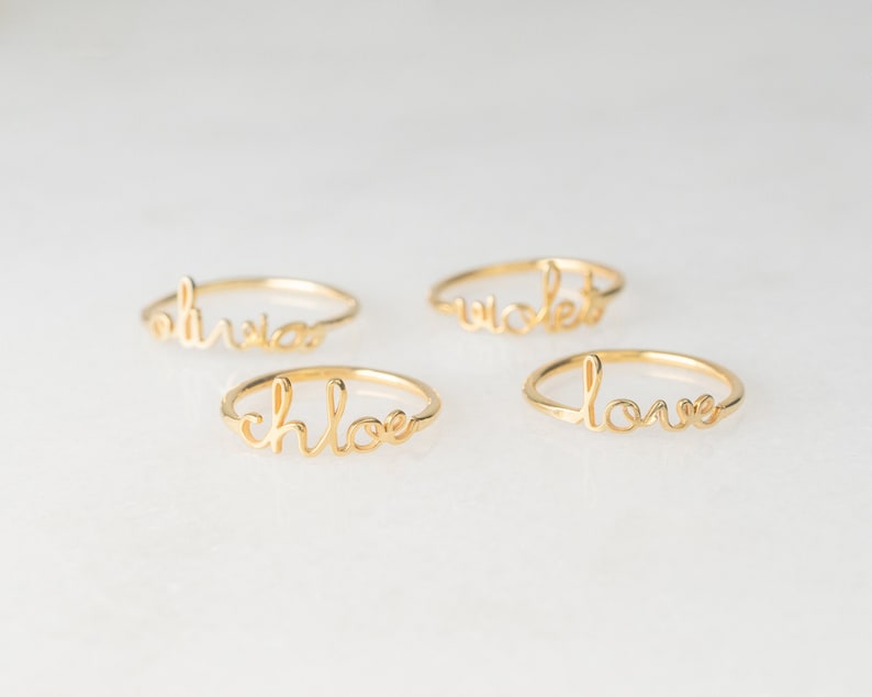 May include: Four gold rings with the words "Olivia", "Chloe", "Violet", and "Love" written in cursive.