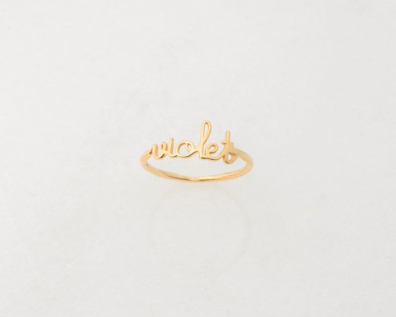May include: A gold ring with the word "violet" written in cursive.