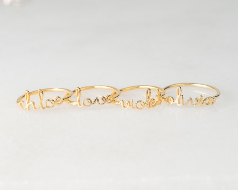May include: Four gold rings with the words "Chloe", "Love", "Nicole", and "Olivia" written in cursive.