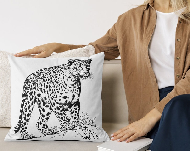May include: A white throw pillow featuring a black and white illustration of a leopard. The leopard is standing on a rock with foliage behind it.