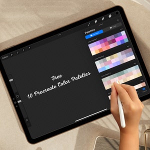 May include: A digital tablet displaying a screen with the text "Free 10 Procreate Color Palettes" and several color palettes. A hand is holding a stylus and hovering over the screen.