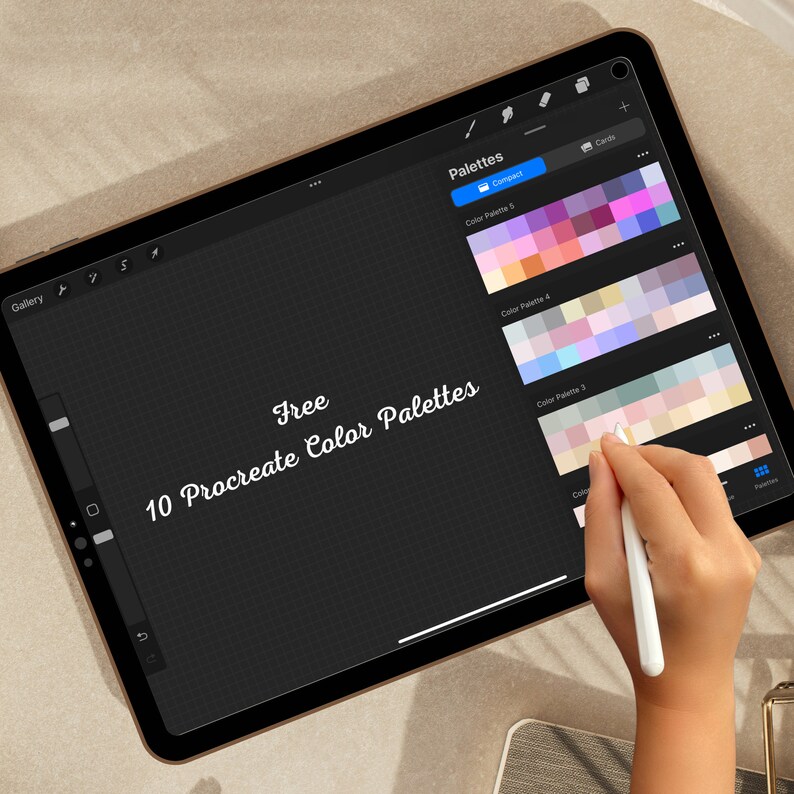 May include: A digital tablet displaying a screen with the text "Free 10 Procreate Color Palettes" and several color palettes. A hand is holding a stylus and hovering over the screen.