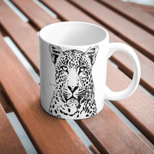 May include: White ceramic mug featuring a black and white illustration of a leopard's face.