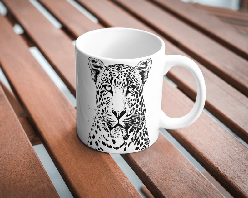 May include: White ceramic mug featuring a black and white illustration of a leopard's face.