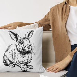 May include: A white throw pillow with a black and white illustration of a rabbit. The rabbit is sitting on its hind legs with its ears perked up.