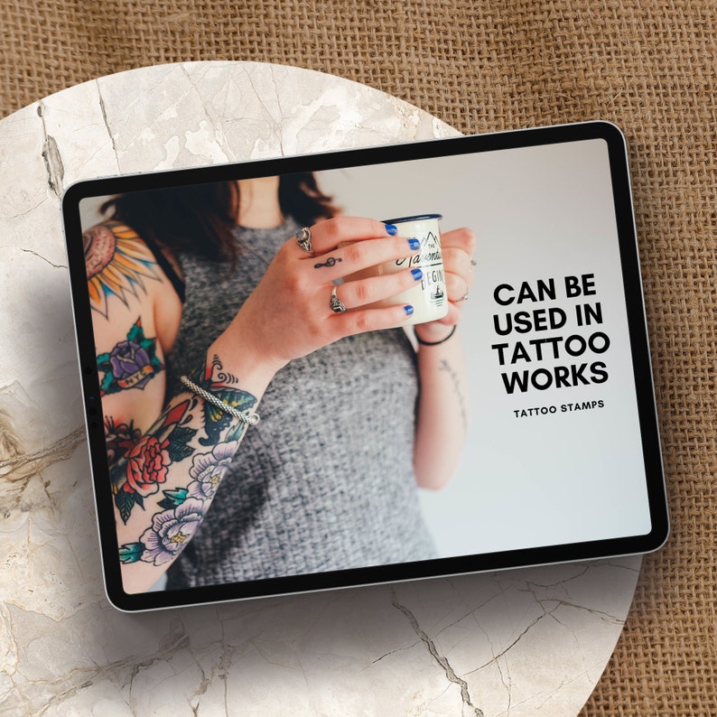 May include: A tablet screen displaying a woman with colorful tattoos on her arm holding a mug. The text on the screen reads "Can be used in tattoo works, Tattoo Stamps."