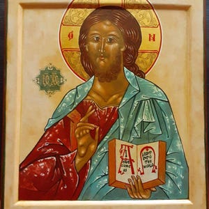 May include: An icon depicting a figure with brown hair and a beard, wearing a teal robe over a red garment. The figure holds an open book with the text "Light into the World" and "Have Come As". A gold halo surrounds the head.