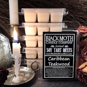 May include: Soy tart melts in clear packaging, labelled "Black Moth Candle Company" with "Caribbean Teakwood" scent. A lit candle and other candles are in the background, creating a warm ambiance.