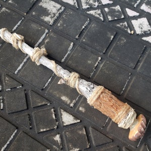 May include: A wooden stick wrapped in twine, with a brown, textured end. The stick is lying on a black and white patterned surface.