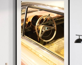 May include: A framed photograph of a vintage car's interior, featuring a brown leather steering wheel and dashboard. The car is parked in a garage or showroom, with a brown leather seat visible in the background.