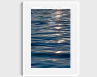 May include: A close-up photo of rippling water with sunlight reflecting on the surface. The water is a deep blue color.