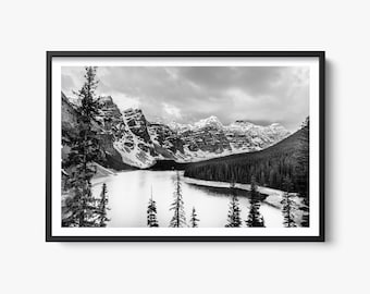 May include: A black and white photograph of a mountain lake with snow-capped peaks in the background. The lake is surrounded by trees and the water is calm and reflective.