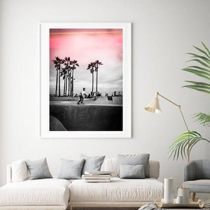 May include: Black and white photograph of a skateboarder in a skate park with palm trees in the background. The sky is a vibrant pink color.