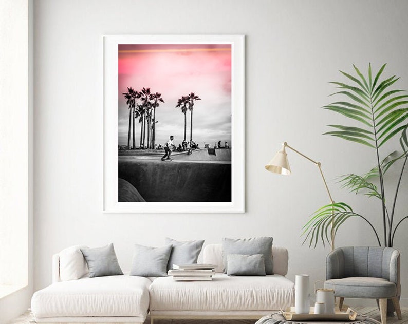 May include: Black and white photograph of a skateboarder in a skate park with palm trees in the background. The sky is a vibrant pink color.
