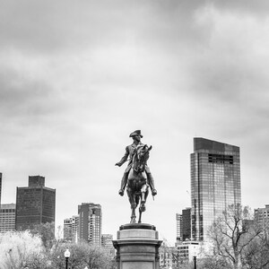 Puede incluir: Una foto en blanco y negro de una estatua de un hombre a caballo en un parque de la ciudad. La estatua est&aacute; en primer plano, y el horizonte de la ciudad est&aacute; en el fondo. La estatua est&aacute; sobre un pedestal, y hay &aacute;rboles y arbustos alrededor.