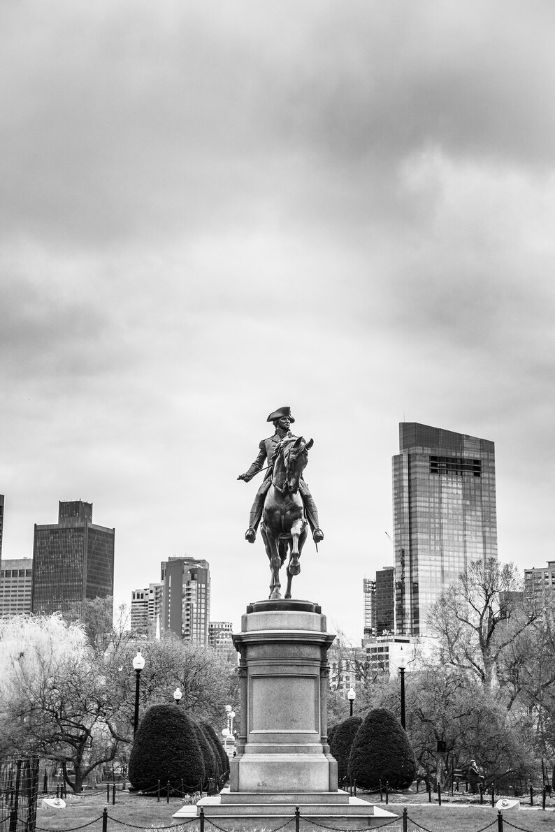 Puede incluir: Una foto en blanco y negro de una estatua de un hombre a caballo en un parque de la ciudad. La estatua est&aacute; en primer plano, y el horizonte de la ciudad est&aacute; en el fondo. La estatua est&aacute; sobre un pedestal, y hay &aacute;rboles y arbustos alrededor.