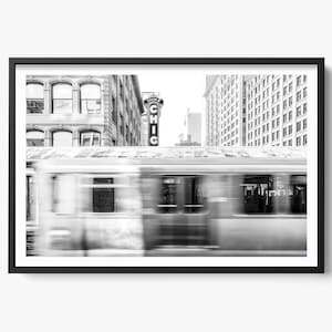 Op de afbeelding: Zwart-wit ingelijste print van een stadsgezicht van Chicago. Een vage trein passeert gebouwen, met het woord "CHIC" zichtbaar op een bord. De afbeelding legt de energie van het stedelijk vervoer vast.