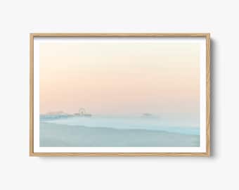 May include: A photograph of a beach with a Ferris wheel and a building in the distance. The beach is covered in fog, and the sky is a soft pink and orange.