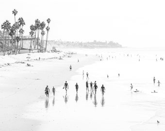 Puede incluir: Una fotografía en blanco y negro de una playa con gente caminando por la orilla. La playa está vacía, excepto por unas pocas personas que caminan por la orilla. El agua está tranquila y el cielo está despejado.