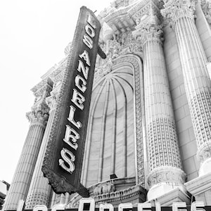 May include: Black and white photo of a building with a large sign that reads "Los Angeles" in neon letters. The building has a classic architectural style with columns and ornate details.