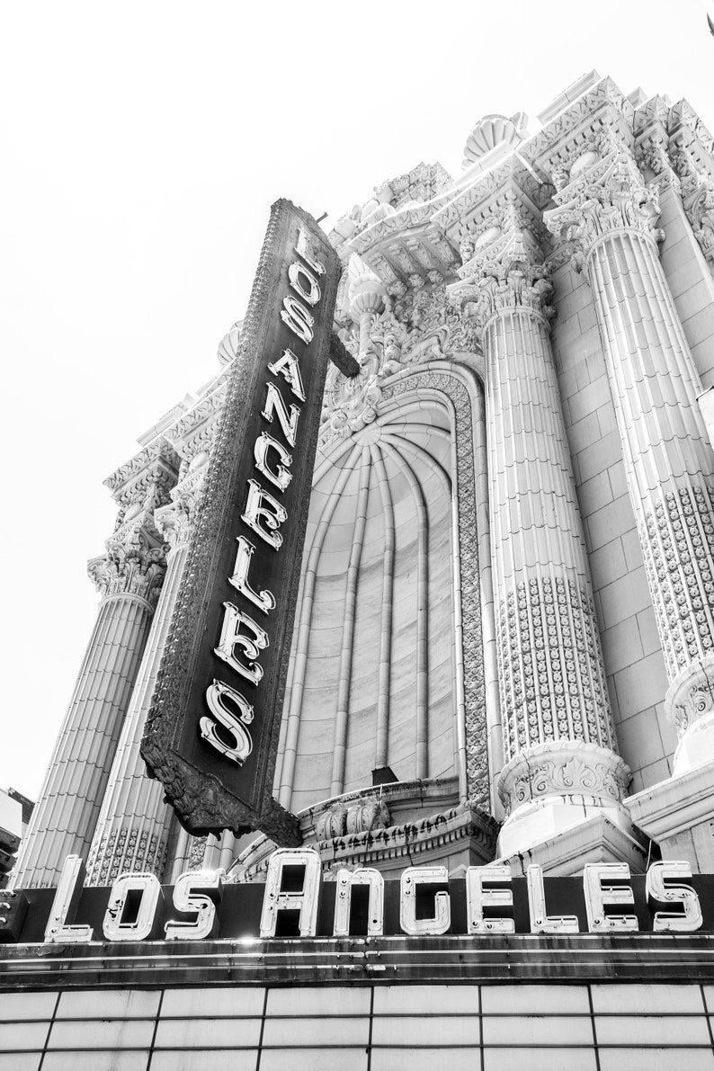 May include: Black and white photo of a building with a large sign that reads "Los Angeles" in neon letters. The building has a classic architectural style with columns and ornate details.