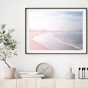 May include: A framed photograph of a beach scene with a soft pink and blue gradient sky and a wave crashing on the shore.