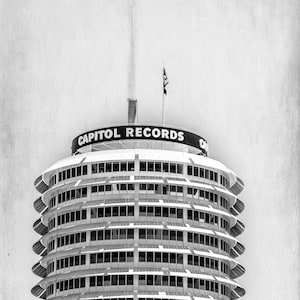 May include: A black and white photo of the Capitol Records building in Los Angeles, California. The building is a round tower with a distinctive, modern design. The building is topped with a spire and a sign that reads "Capitol Records".