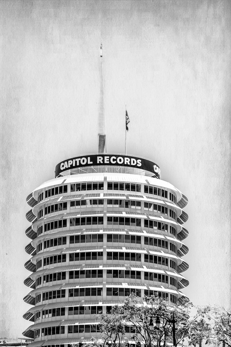 May include: A black and white photo of the Capitol Records building in Los Angeles, California. The building is a round tower with a distinctive, modern design. The building is topped with a spire and a sign that reads "Capitol Records".