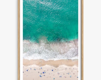 May include: An aerial view of a beach with turquoise water and white sand.  People are scattered across the beach with blue umbrellas.