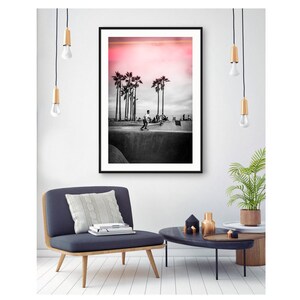 May include: Black and white photograph of a skateboarder in a skate park with palm trees in the background. The sky is a vibrant pink.