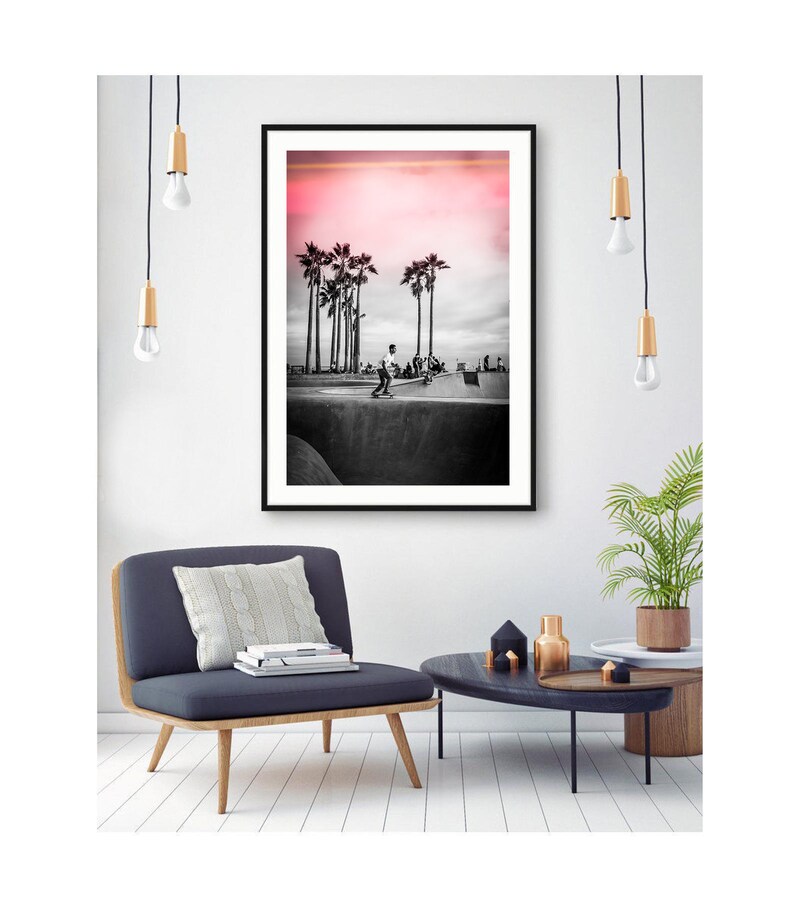 May include: Black and white photograph of a skateboarder in a skate park with palm trees in the background. The sky is a vibrant pink.