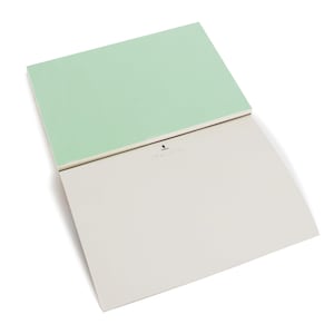 May include: A blank, light green notepad with a white, lined interior. The notepad is folded in half and the top half is visible. The notepad has a small, black logo on the front.