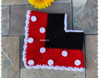 May include: A red and black crocheted baby blanket with white polka dots and a white crocheted border. The blanket is on a stone surface with a sunflower in the background. The text "Esther C." is visible on the blanket.