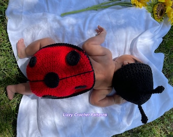 May include: A baby wearing a red and black crocheted ladybug costume with a matching hat. The baby is lying on a white blanket on a bed of green grass. The text "Lizzy Crochet Patterns" is visible in the bottom center of the image.