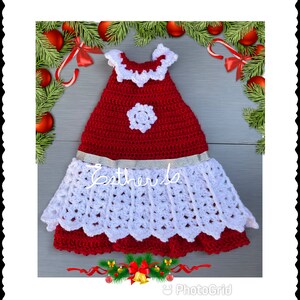 Puede incluir: Un vestido de crochet rojo y blanco con un dise&ntilde;o de copo de nieve y una cinta plateada. El vestido tiene un dobladillo festoneado y un escote con volantes.