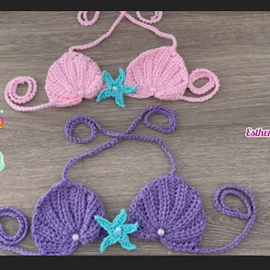 May include: Two crocheted mermaid shell bikini tops, one pink and one purple, with a turquoise starfish embellishment on each. The tops have adjustable straps and are made with a soft yarn.