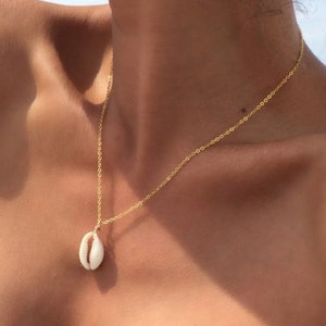 Könnte beinhalten: Eine goldene Kettenkette mit einem weißen Muschel-Anhänger.