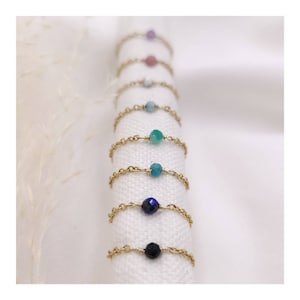 Puede incluir: Un conjunto de anillos de cadena de oro con cuentas de piedras preciosas de diferentes colores. Los anillos se muestran sobre un fondo de tela blanca.