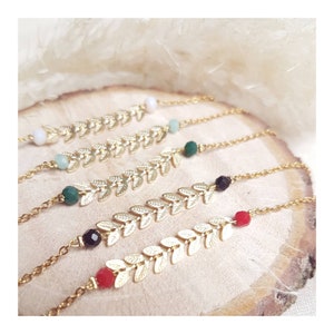 Peut inclure: Cinq bracelets en chaîne à feuilles d'or avec des perles de différentes couleurs. Les perles sont rouges, noires, vertes et bleu clair.