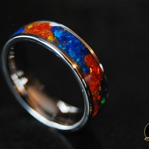May include: A silver band ring with a colorful inlay of red, blue, and green gemstones. The ring is polished and has a smooth finish.