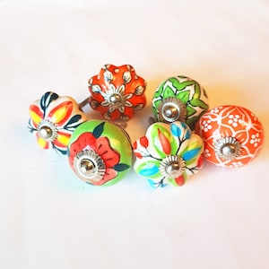 May include: Six colorful ceramic drawer knobs with floral designs. The knobs are in shades of green, orange, red, yellow, and blue.