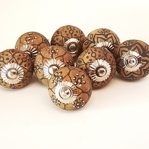 May include: Eight brown ceramic cabinet knobs with intricate black and orange designs. Each knob has a silver metal base.